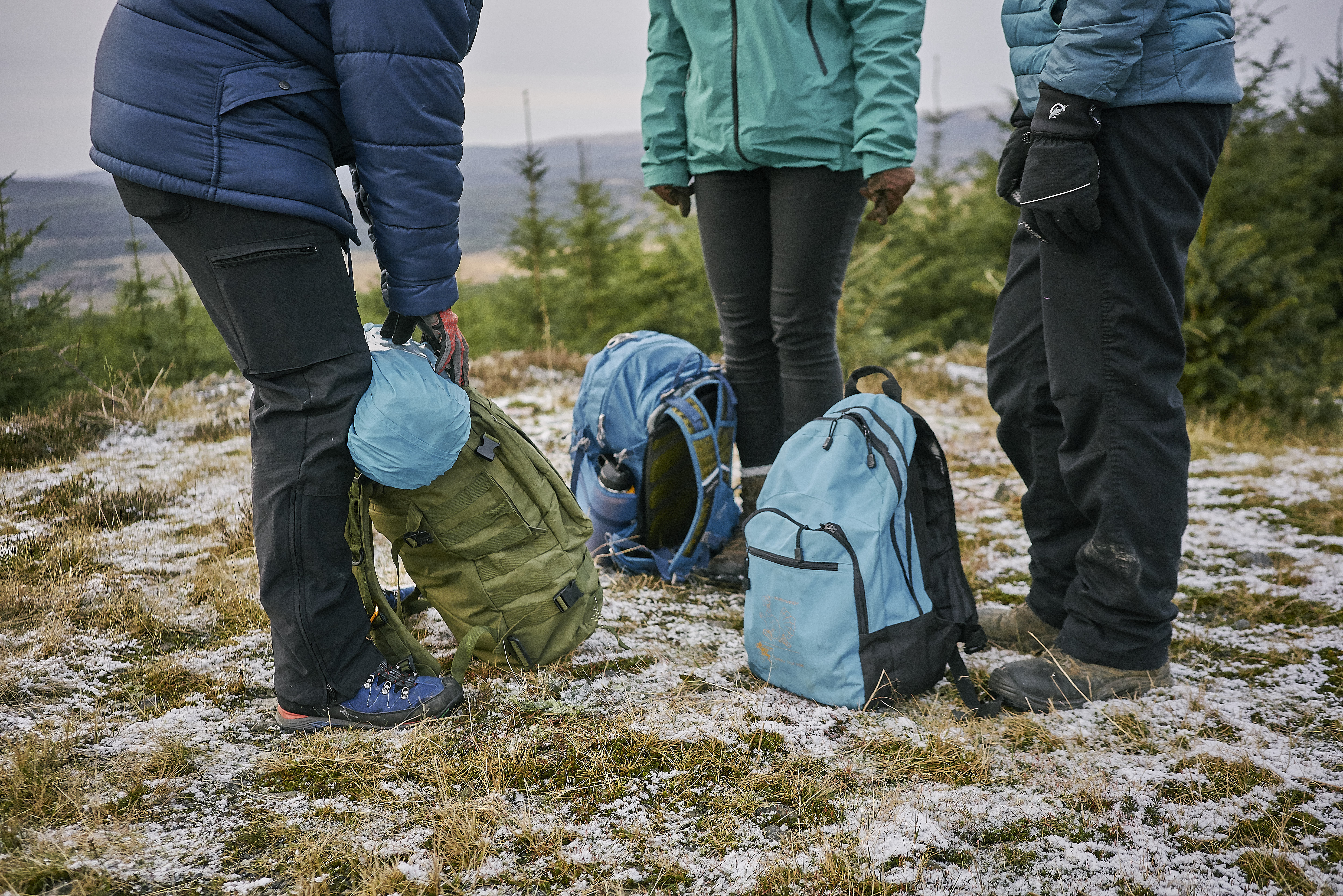 Three people with rucksacks, standing on a hill
