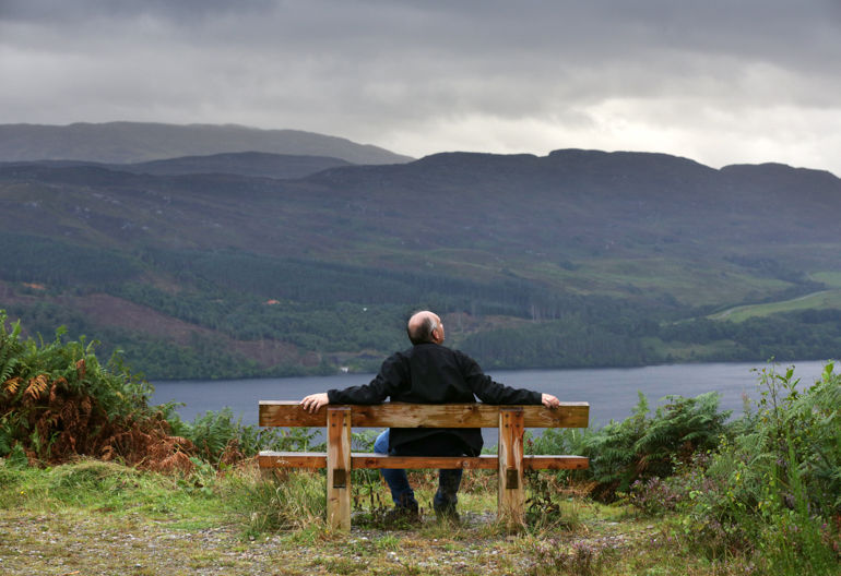 Man takes in view over Loch Ness, from wooden bench at Allt na Criche, near Fort Augustus