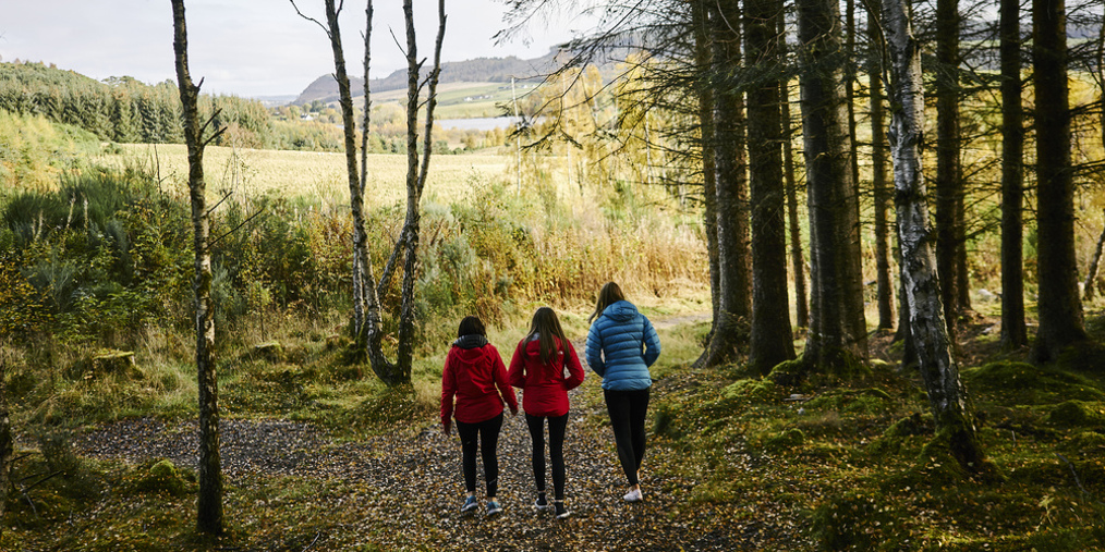 Three women in jackets walking on a forest path