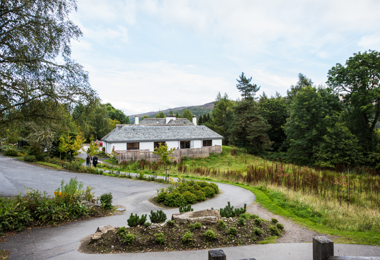 Low white building with car park and trees beside.