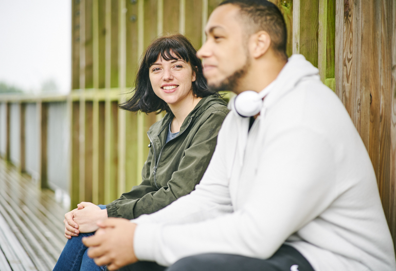 A man and woman sit on a bench inside a wooden structure