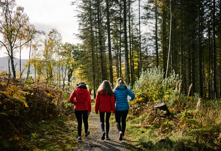 Rear view of woman and two teenage girls walking along woodland trail, Contin Forest, near Strathpeffer, with Strathconon hills in background
