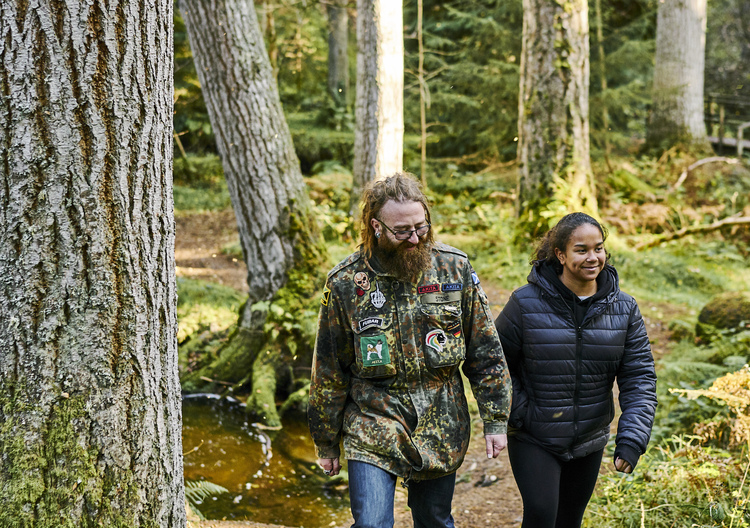 Man wearing combat jacket and dreadlocks and teenage girl walk on woodland path, near the Clootie Well, Munlochy, Black Isle