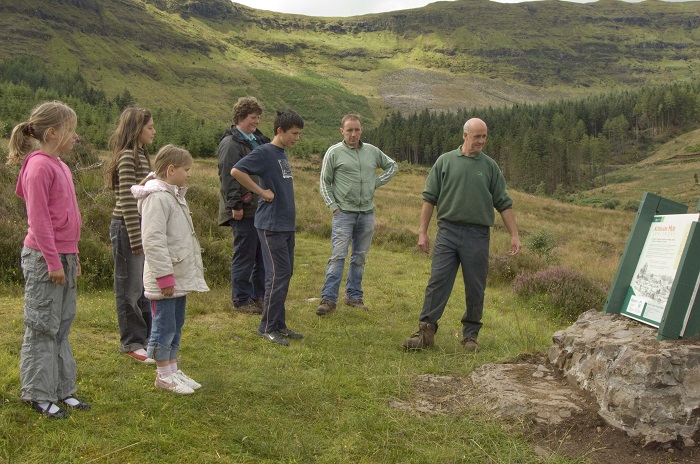 Group of people standing on grassy hillside reading a large sign