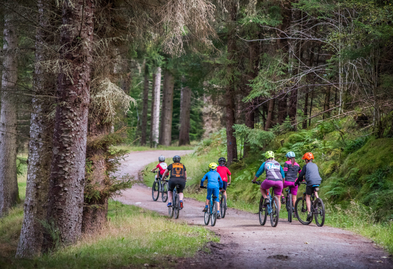 Rear view of group of women and small boys on mountain bikes ride on cycle path, Balnain near Loch Ness
