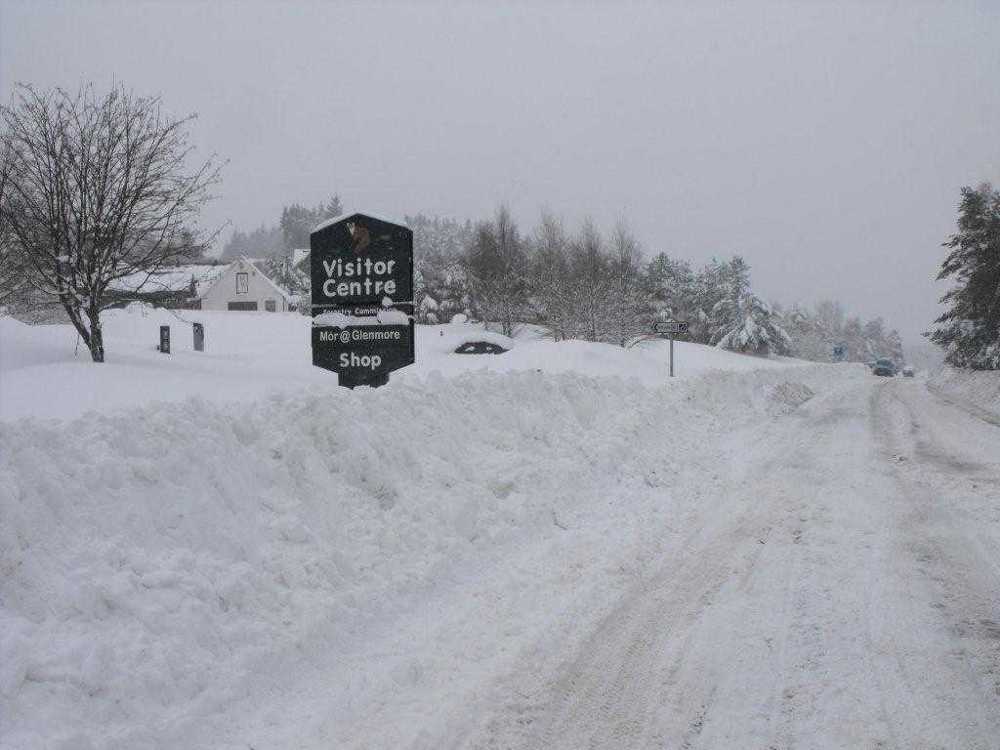 Snowy road with large snow banks on either side with the visitor centre in the background.