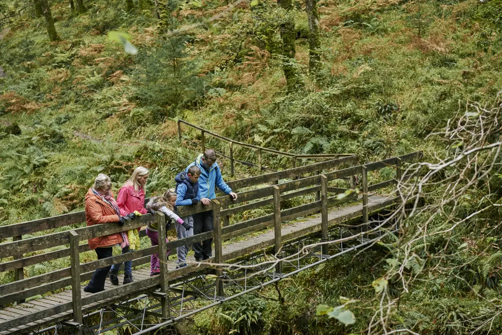 Man and two women with one male and one female child on a bridge above a river in Glenbranter