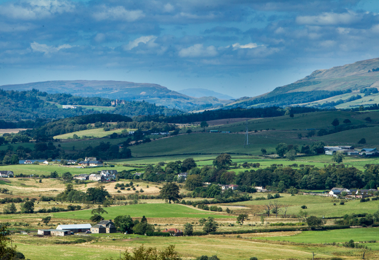 View of a valley with small farms and houses scattered throughout it and hills in the background