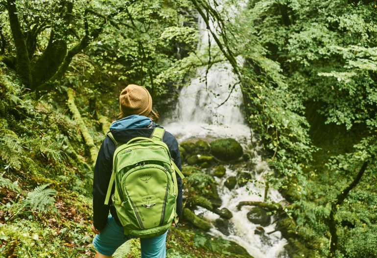 Young woman hiker carrying haversack views waterfall, Glen Creran, near Glencoe